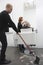 Man Sweeping While Hairdresser Giving Haircut To Senior Woman