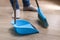 The man sweeps the debris into a blue scoop with brush.