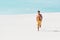 Man in swim shorts with muscular torso running on sandy beach