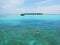 Man swimming in Maldives blue sea water near a tropical resort and traditional Maldivian boat in the background.