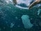 A man swimming among toxic plastic wastes floating in the ocean