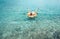 Man swims on inflatable pineapple pool ring in crystal clear sea