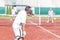 Man swinging racket while playing tennis doubles on red court during summer weekend