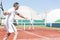 Man swinging tennis racket while playing doubles match on red court during summer weekend