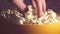A man takes fresh hot popcorn from a bowl. A male hand picks popcorn from a bucket.