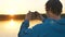 Man takes panorama of nature at sunset on smartphone sitting in kayak on calm lake, outdoor activities