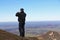 A man takes a picture of the view down a mountain with his mobile phone