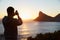 Man Taking Picture Of Sun Setting Over Sea On Mobile Phone