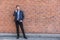 Man talking business on phone holding smartphone in city street in smart casual wear standing against brick wall urban background