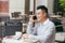 Man talking on the mobile phone in a coffee shop sitting in the terrace outdoors and holding a cup - Image