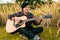 Man in tartan shirt wearing headset and playing guitar of string song on gold rice field in the evening