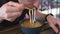 Man tastes soup in black bowl sitting at brown cafe able