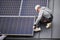 Man technician mounting photovoltaic solar panels on roof of house with help of hex key.