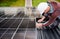 Man technician mounting photovoltaic solar panels on roof of house with help of hex key.