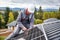 Man technician mounting photovoltaic solar panels on roof of house with help of hex key.