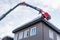 Man in the telescopic aerial platform cleaning snow and ice from roof top, gutter of the buliding to avoid the danger