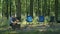 Man tending to a campfire in a serene forest setting with empty camping chairs. Outdoor relaxation and camping lifestyle
