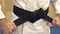 Man ties a black belt on a white kimono.