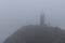 man on top of a mountain at a lighthouse in the fog