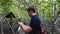 Man Tourist with Backpack Makes Video on Smartphone in Green Mangroves Forest