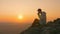 Man tourist sits sitting on edge of cliff, drinks tea from mug, enjoying sunset