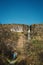 Man tourist standing on a foot path in a forest hands up. Devil`s chimney waterfall in the background. Warm sunny day. Travel and