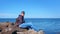 Man tourist traveller admires seascape sitting huge cobblestone on sea shore.