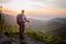 Man tourist with trekking poles on top of hill at sunrise