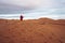 Man in traditional clothes with sandboard standing on sand dunes against sky