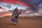 Man in traditional clothes with sandboard walking on sand dunes against sky