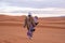 Man in traditional clothes with sandboard walking on sand dunes against sky