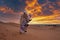 Man in traditional clothes with sandboard walking on sand dunes against sky