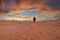 Man in traditional clothes with sandboard walking on sand dunes during dusk