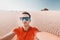 Man tramp in sunglasses takes a selfie photo in the desert against the background of a dune of white sand