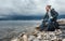 Man traveler with a backpack seets on the seashore against a background of clouds and a mountain range concept of hiking