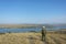 Man traveler in hat on mountain top looks at river below against blue sky. Copy space, soft focus. Freedom and travel concept