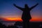 Man traveler silhouette hiking at sunset on Santorini island. Happy tourist raised arms feeling free, admiring landscape