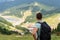 Man traveller with backpack standing on peak and looking on valley