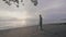 Man treasure hunter with a metal detector works on the ocean sand beach at sunset.