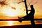 Man on tree. Silhouette of lone man sit on branch of birch tree at sunset at shoreline.