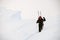 man with trekking poles walks through deep powdery snow on a mountain slope