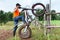 Man with trial mototrcycle training in countryside area, raising bike on rear wheel, leaning against wooden fence