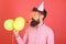 Man with trimmed beard wearing pink shirt and party cap isolated on red background. Bearded man blowing party whistle