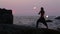 Man turns fire poi standing on a cliff near the ocean at sunset