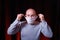A man tying a medical gauze mask on dark red background. Emotion of surprise. Virus preventive methods