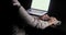 Man is typing on the keyboard looking at laptop screen sitting at the table on workplace in the dark. Hands close-up.