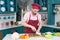 Man in uniform apron cutting zucchini on slice by knife. Orange and red paprika on table prepared for cutting after green zucchini