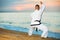 Man in uniform doing taekwondo exercises at sunset sea shore