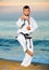 Man in uniform doing taekwondo exercises at sunset sea shore