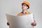 Man in uniform looking in opened paper building plan on grey background. Construction worker in protective helmet on head and
